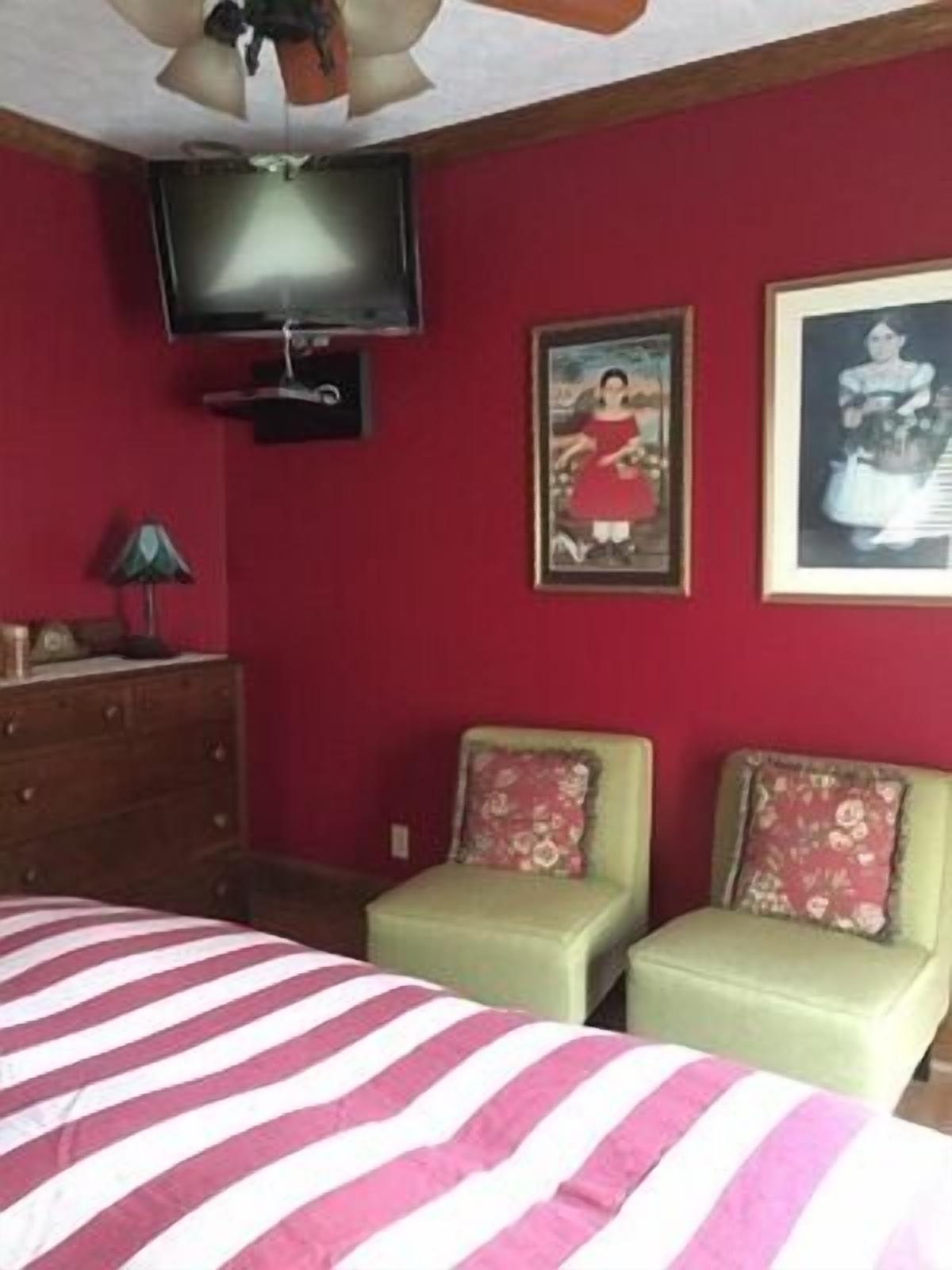 A bedroom with a bed, two chairs, a dresser, a television, and two framed pictures on the wall.