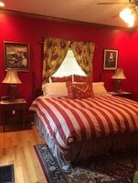 Un dormitorio con una cama grande, paredes rojas y cortinas con estampado floral.