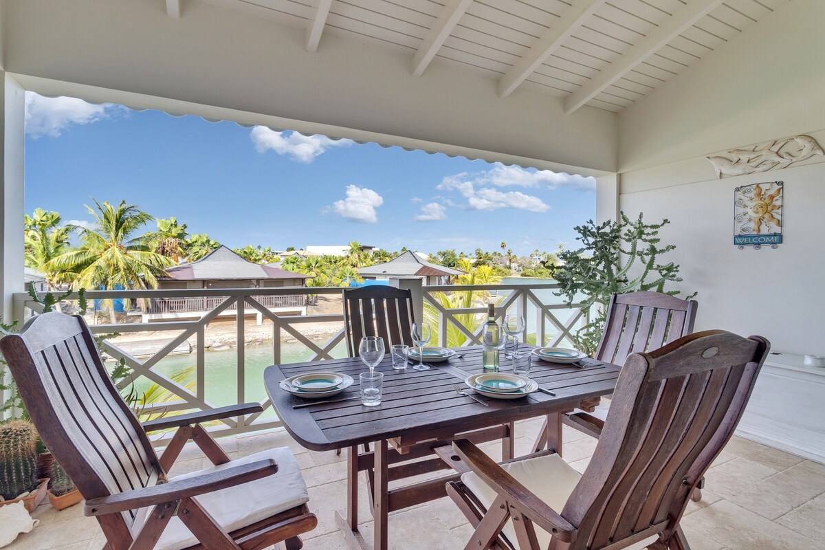 A covered outdoor dining area with a table set for four, overlooking a pool and palm trees.