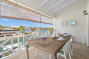 A wooden dining table set with white chairs and plates, overlooking a marina with boats and houses.