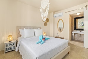 A hotel room with a large bed, bedside lamps, a vanity with a mirror, and an air conditioning unit.