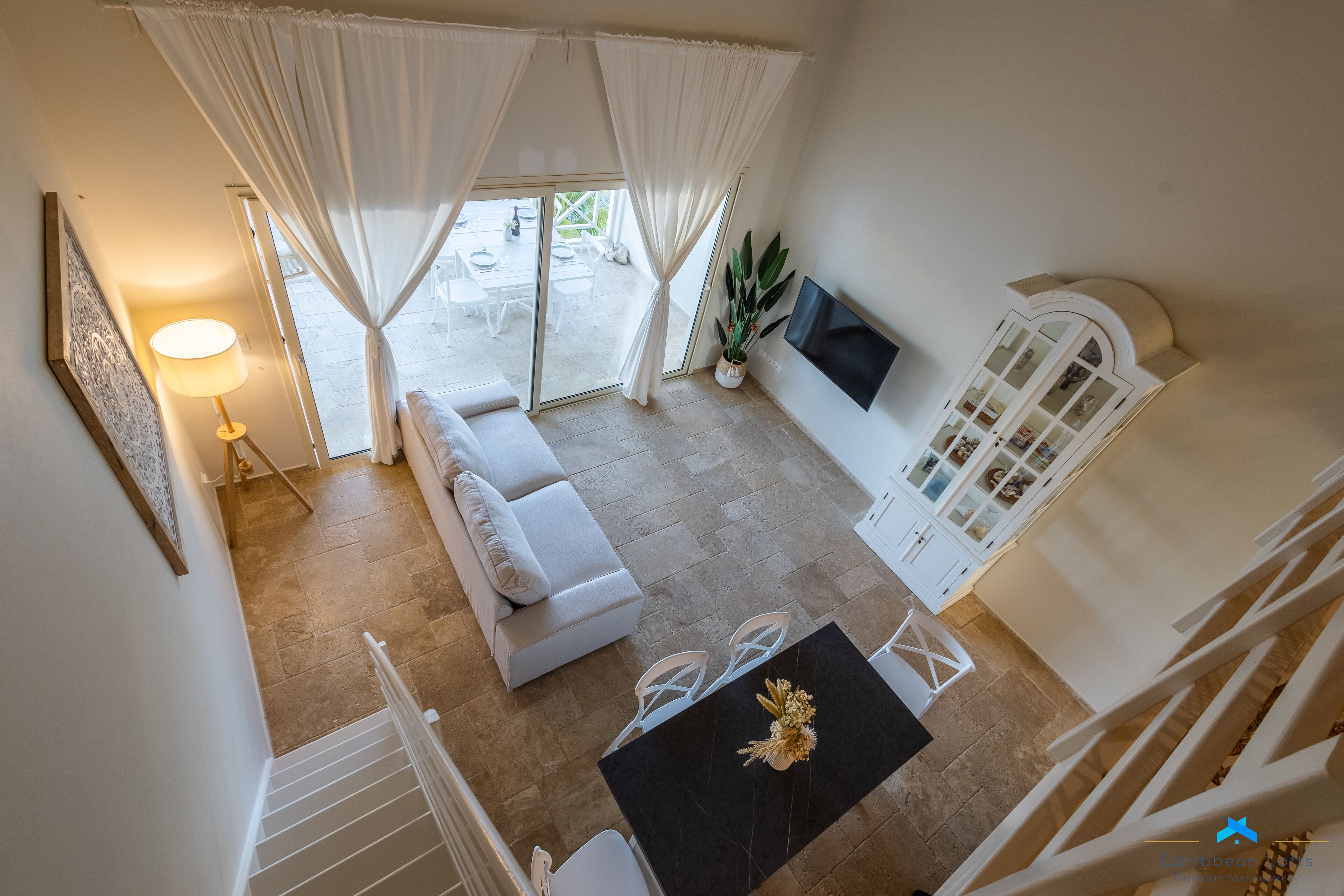 A spacious living area with a sofa, a dining table with chairs, a TV mounted on the wall, and a staircase leading to another level.