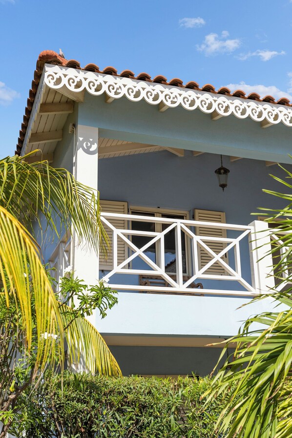 A light blue building with a white balcony railing, a tiled roof, and a small balcony with a lantern.