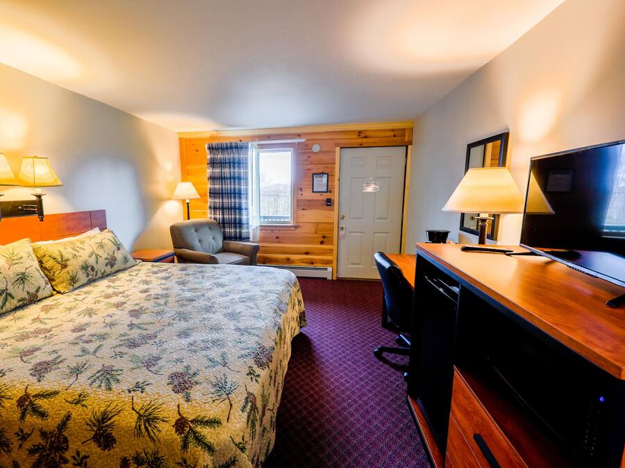 A hotel room with a bed, a desk, a chair, a television, and a window with curtains.