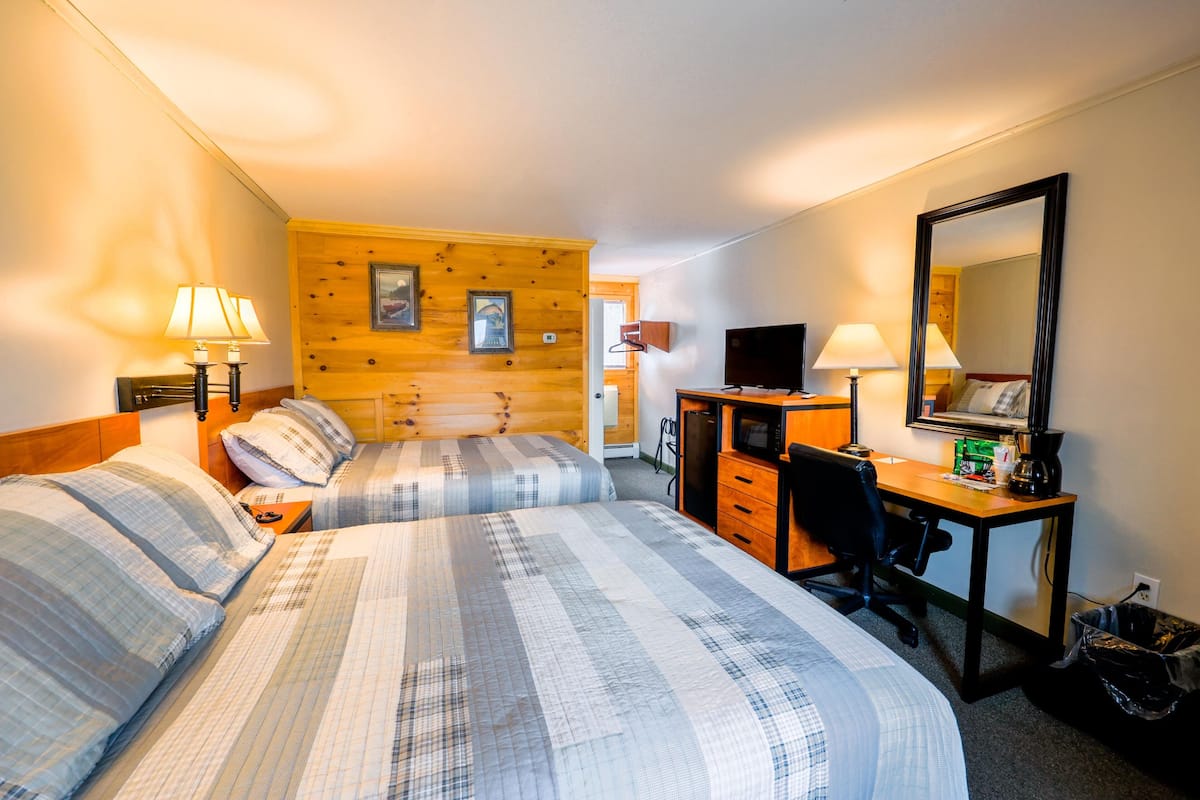 Quarto de hotel com duas camas, uma escrivaninha, uma cadeira, uma televisão e um espelho.