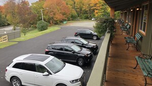 A parking area with several cars, a covered walkway with benches, and a view of autumn-colored trees.