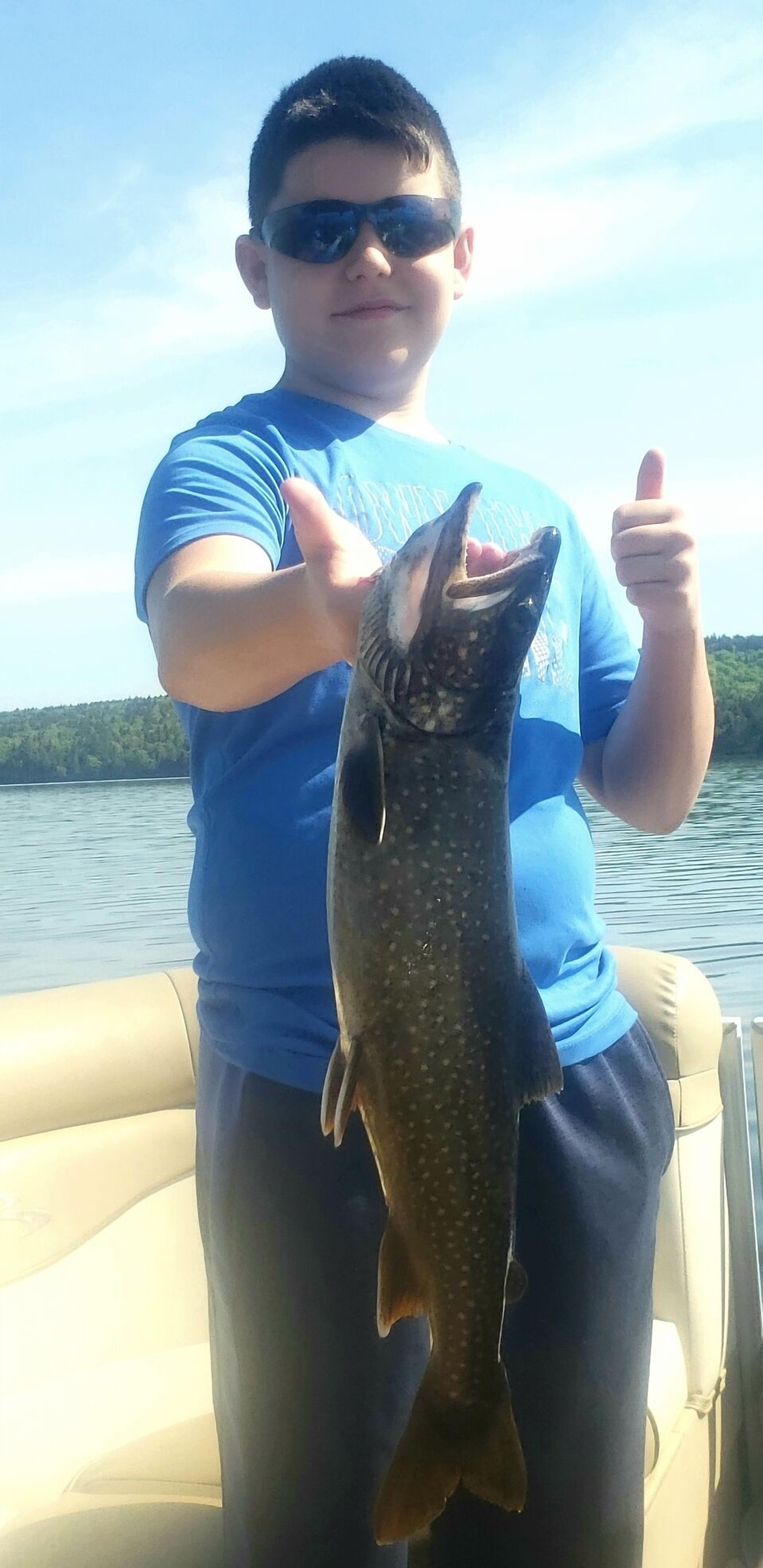 A person holding a fish on a boat with a lake and trees in the background.
