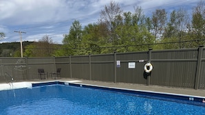 A rectangular swimming pool with a clear blue water surface, surrounded by a dark fence.