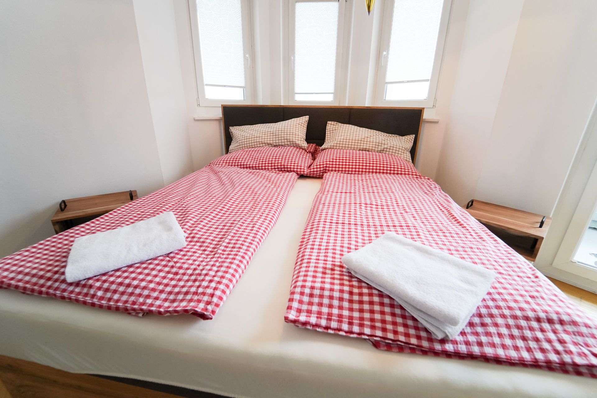 A double bed with red and white checkered bedding, two pillows, and a white towel on each side.
