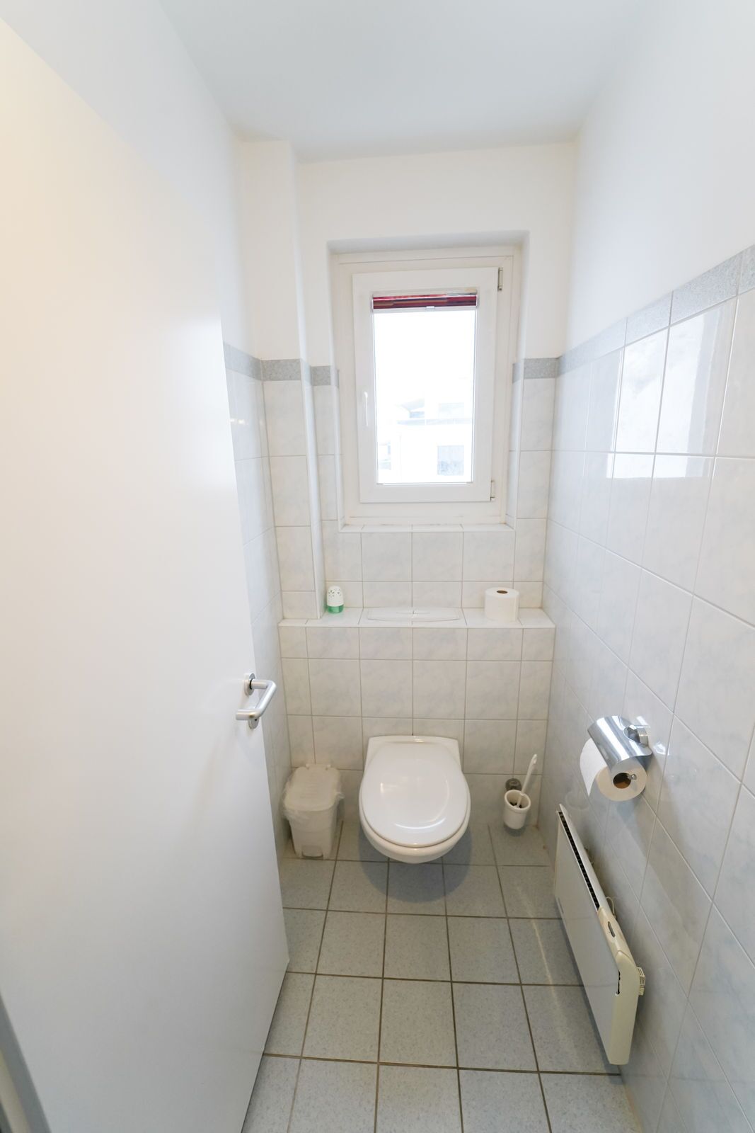 Une petite salle de bain propre, équipée de toilettes, d’une fenêtre et d’un porte-serviettes.