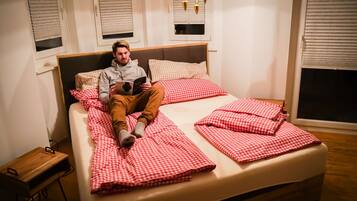 Une personne allongée sur un lit avec une couette à carreaux, une tête de lit en bois et une table de chevet avec une lampe.