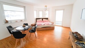 A small, bright room with a bed, a dining table with chairs, and a large window. - Schlafgut Küssler Zell am See (Zell am See)