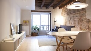 Ein modernes Wohnzimmer mit Esstisch, Stühlen, Fernseher und einem großen Fenster.