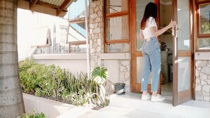 A woman standing at a glass door with a stone wall and wooden beams. - Lighthouse Guesthouse & Cafe (Groblersdal)