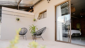 A balcony with two black wire-framed chairs, a potted plant, and a sliding glass door leading to a bedroom with a bed and a nightstand. - Lighthouse Guesthouse & Cafe (Groblersdal)