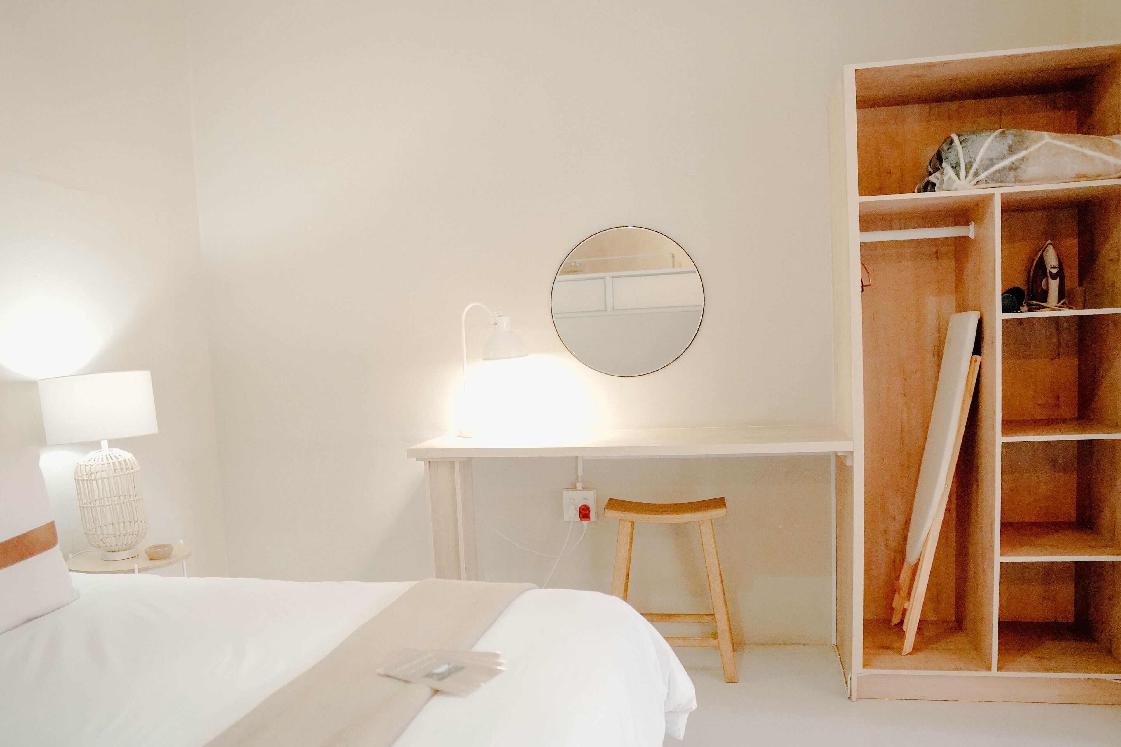 Een hotelkamer met een bed, een bureau met spiegel, een stoel en een houten garderobe.