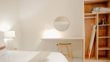 Een hotelkamer met een bed, een bureau met spiegel, een stoel en een houten garderobe.