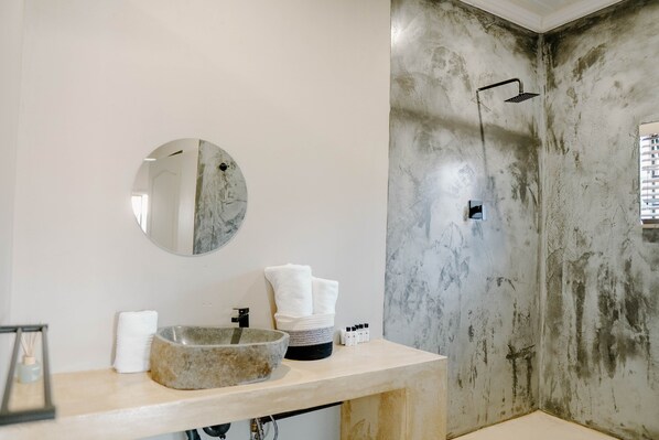 A bathroom with a round mirror, a stone basin, a towel, and a shower with a textured wall. - Lighthouse Guesthouse & Cafe (Groblersdal)