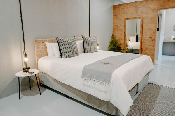 Un dormitorio moderno con una cama grande, una mesita auxiliar pequeña, un espejo y una planta.