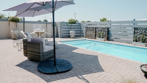 A poolside area with a seating arrangement, a covered umbrella, and a stone wall. - Lighthouse Guesthouse & Cafe (Groblersdal)