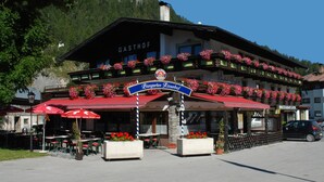 A traditional Bavarian Gasthof with outdoor seating, red awnings, and flower boxes.
