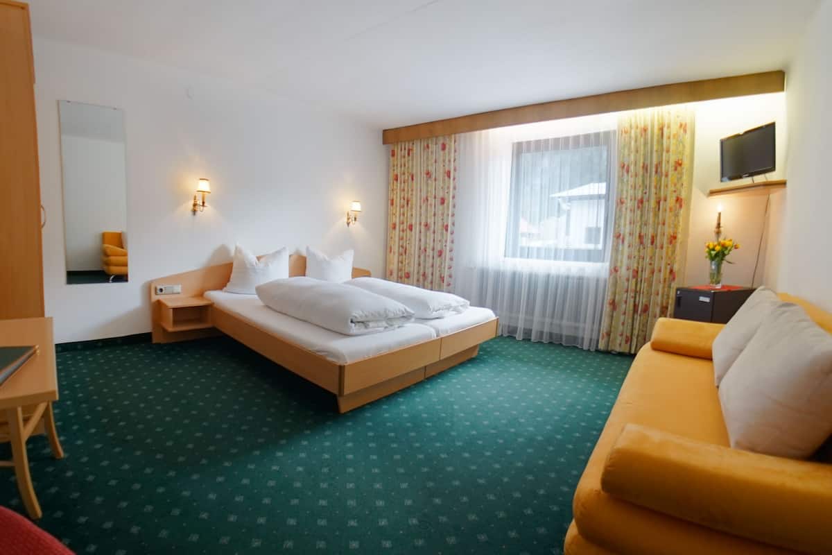 A hotel room with a bed, a desk, a chair, a TV, and a window with curtains.