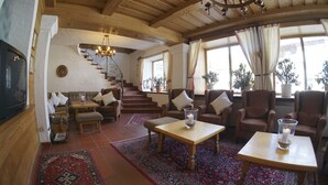 A cozy living room with a fireplace, comfortable seating, a staircase, and large windows with curtains.