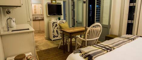 A hotel room with a bed, a desk, a chair, a television, and a small kitchenette.
