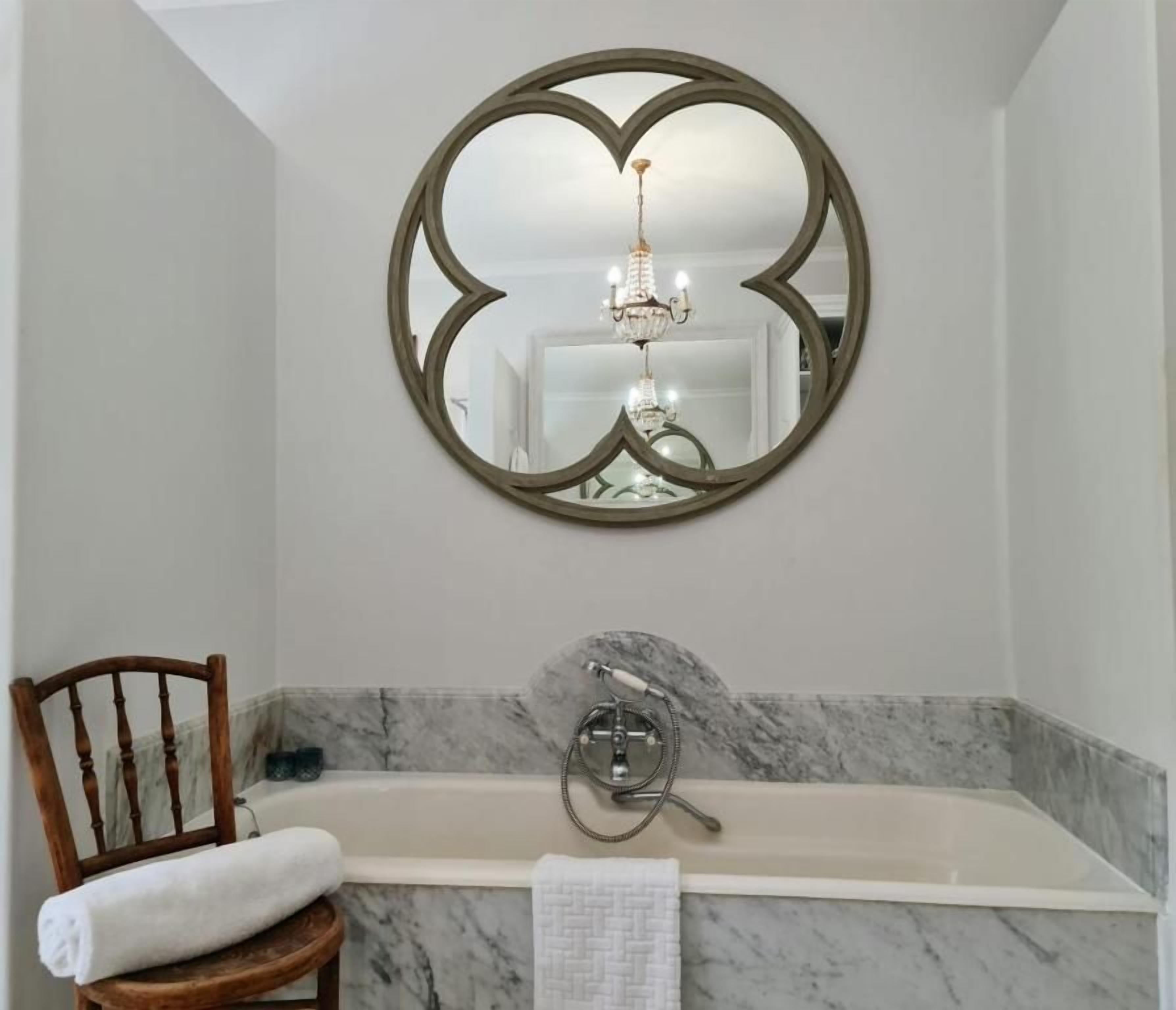 A bathroom with a marble sink, a freestanding bathtub, a wooden chair with a towel, and a mirror with a unique frame.