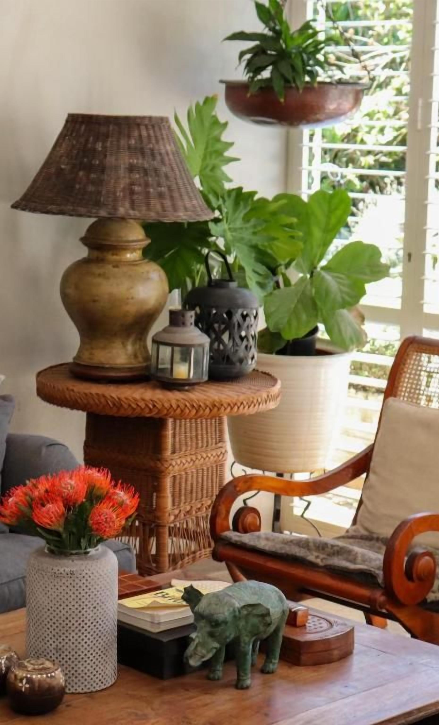 A room with a wicker table, a lamp, a potted plant, a chair, and a small decorative animal.