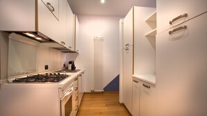 A narrow kitchen with white cabinets, a stove, and a radiator. - Verona For Rent Blu Theater (Verona)