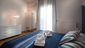 A hotel room with a bed, two towels, a dresser, a lamp, and a radiator. - Verona For Rent Blu Theater (Verona)