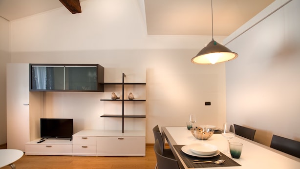 A modern kitchen with white cabinetry, a built-in TV, and a dining area with a long table and chairs. - Verona For Rent Blu Theater (Verona)