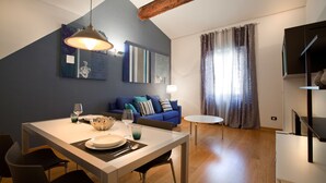 A modern living room with a dining area, featuring a blue sofa, a white table, and a ceiling with exposed beams. - Verona For Rent Blu Theater (Verona)