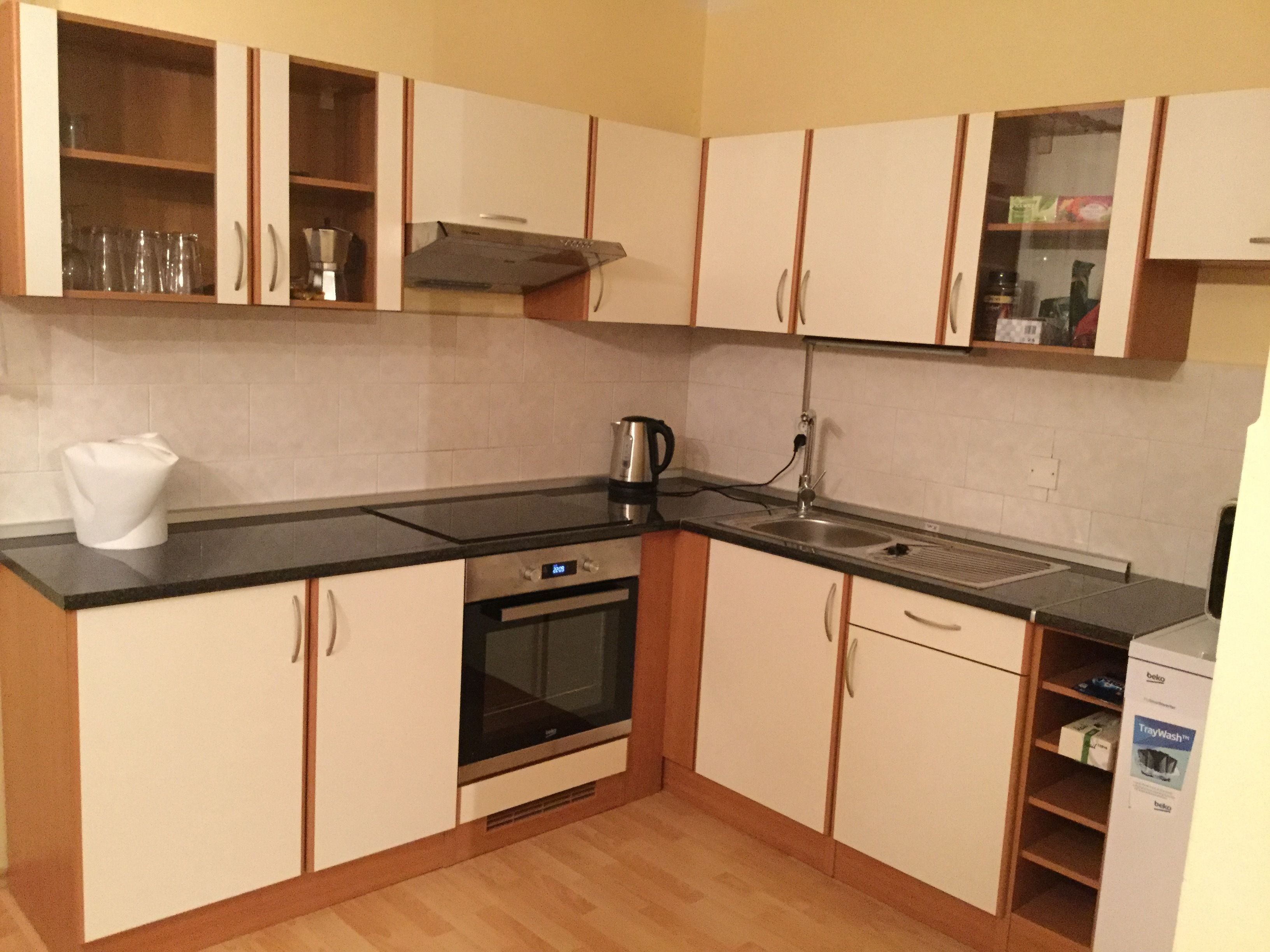 Een kleine keuken met een zwart aanrecht, roestvrijstalen apparatuur en houten kastjes.