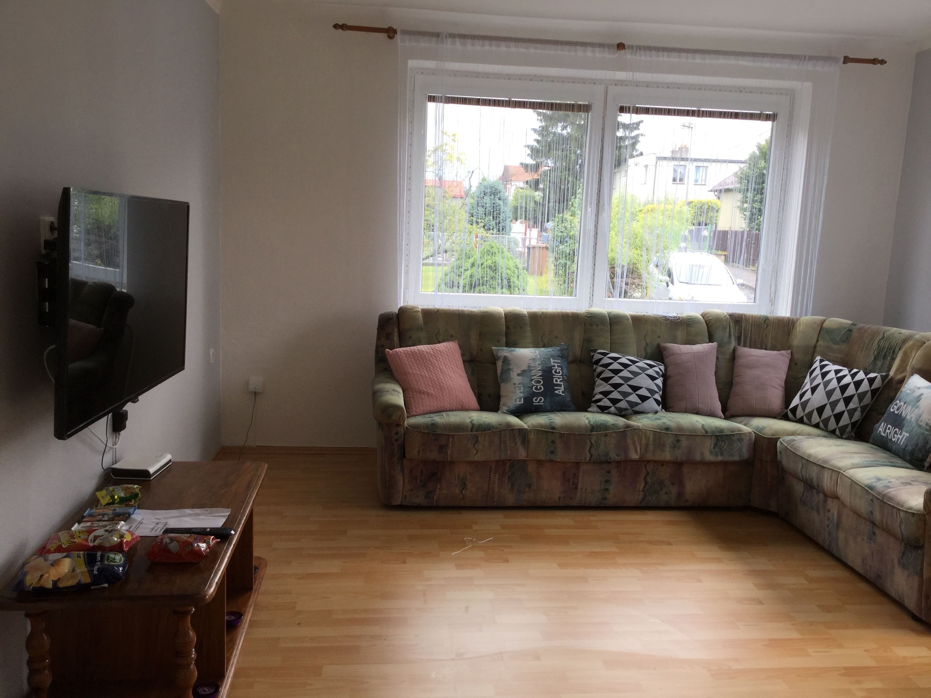 A living room with a sectional sofa, a flat-screen TV mounted on the wall, and a wooden coffee table with snacks.