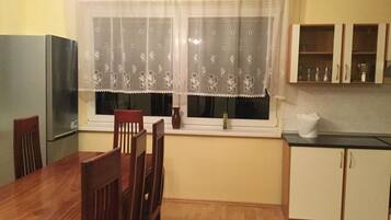A dining area with a wooden table and chairs, a window with patterned curtains, and a kitchen with cabinets and a countertop.