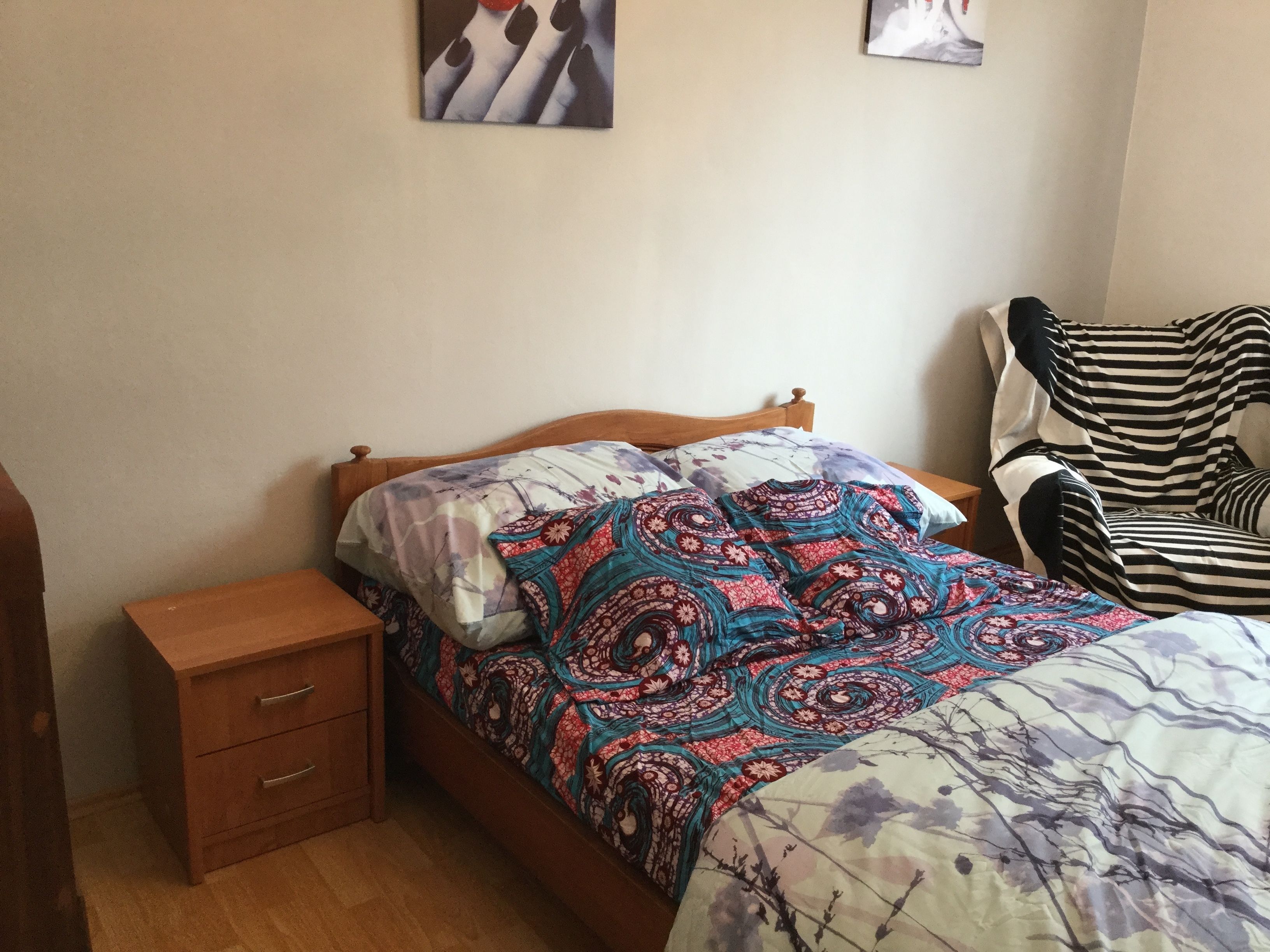 Une chambre à coucher avec un lit en bois, une table de chevet, une chaise à rayures et un mur orné de deux tableaux encadrés.