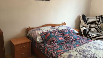 Une chambre à coucher avec un lit en bois, une table de chevet, une chaise à rayures et un mur orné de deux tableaux encadrés.
