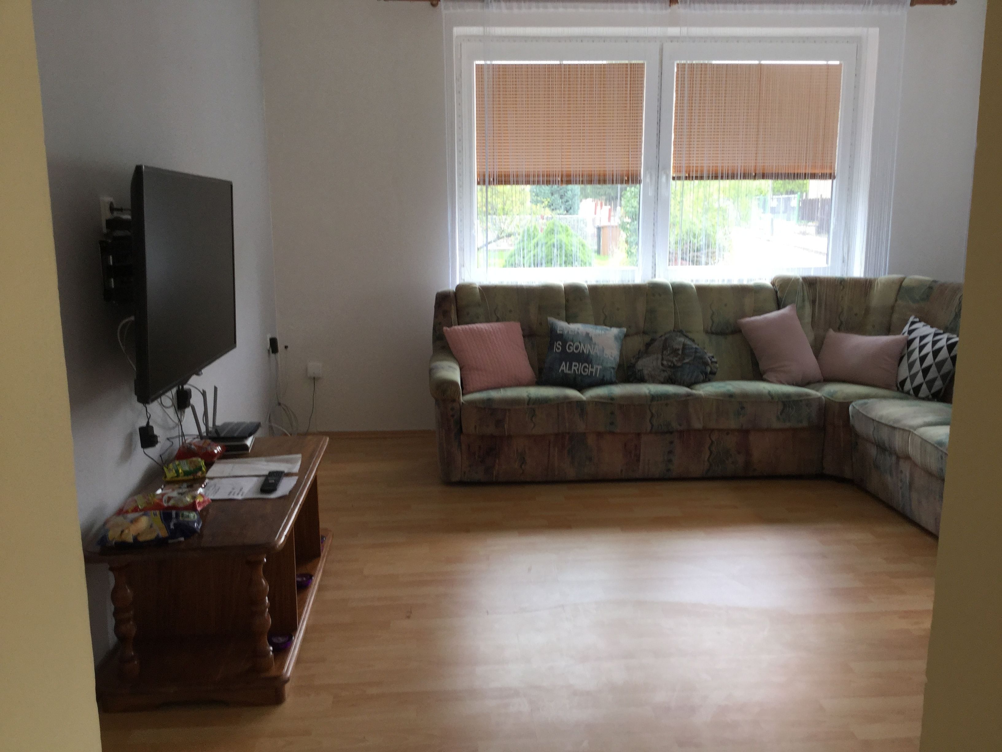 Een woonkamer met een hoekbank, een flatscreen televisie aan de muur en een houten salontafel.