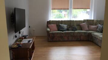 Een woonkamer met een hoekbank, een flatscreen televisie aan de muur en een houten salontafel.