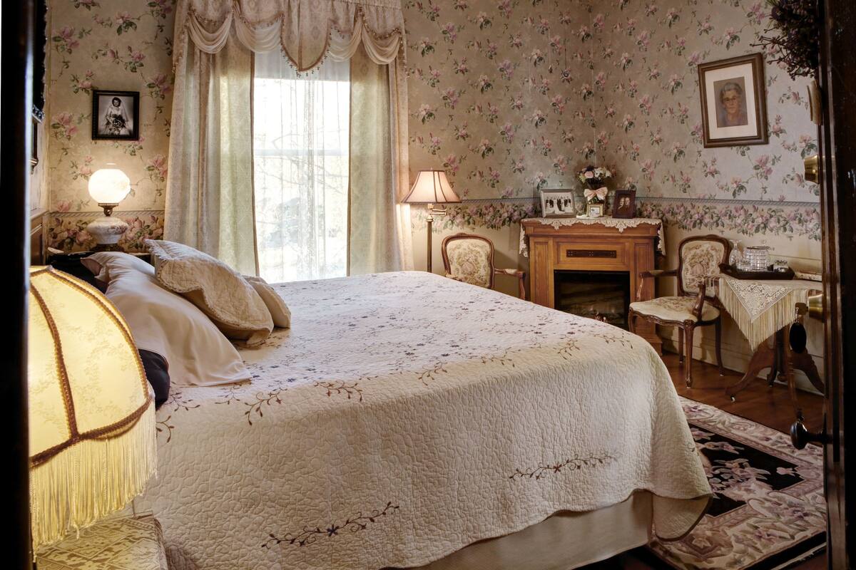 A bedroom with a large bed, two bedside tables with lamps, a wooden dresser, and a chair.
