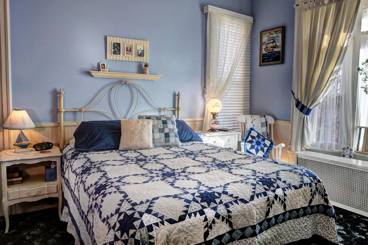 A bedroom with a bed, nightstands, a window with curtains, and wall decorations.