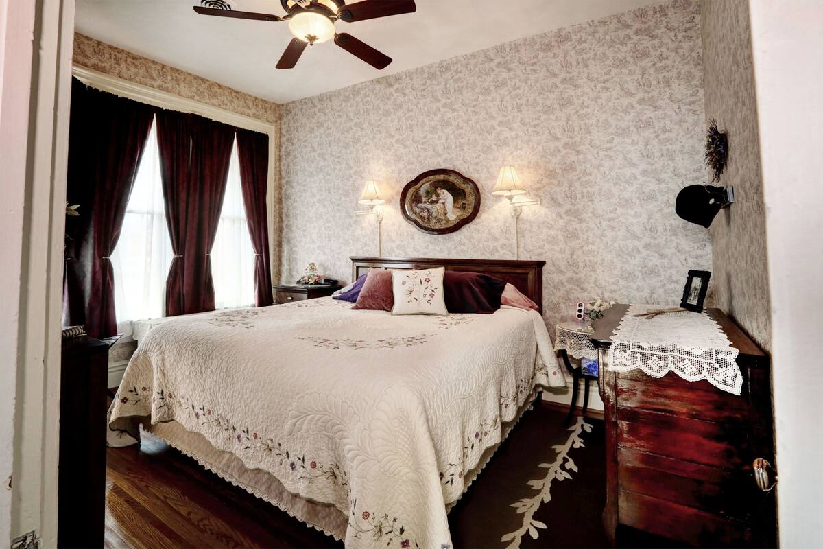 A bedroom with a large bed, a wooden dresser, a nightstand, and a ceiling fan.