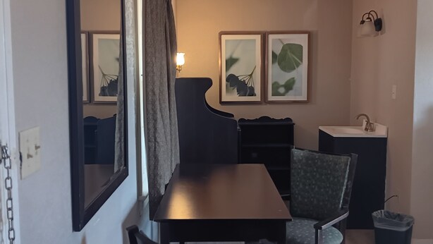 A room with a dark wooden table, two chairs, a small sink, and a trash bin. There are two framed pictures on the wall. - Sheldon's Motel by OYO Keysville Near Hwy 360 (Keysville)