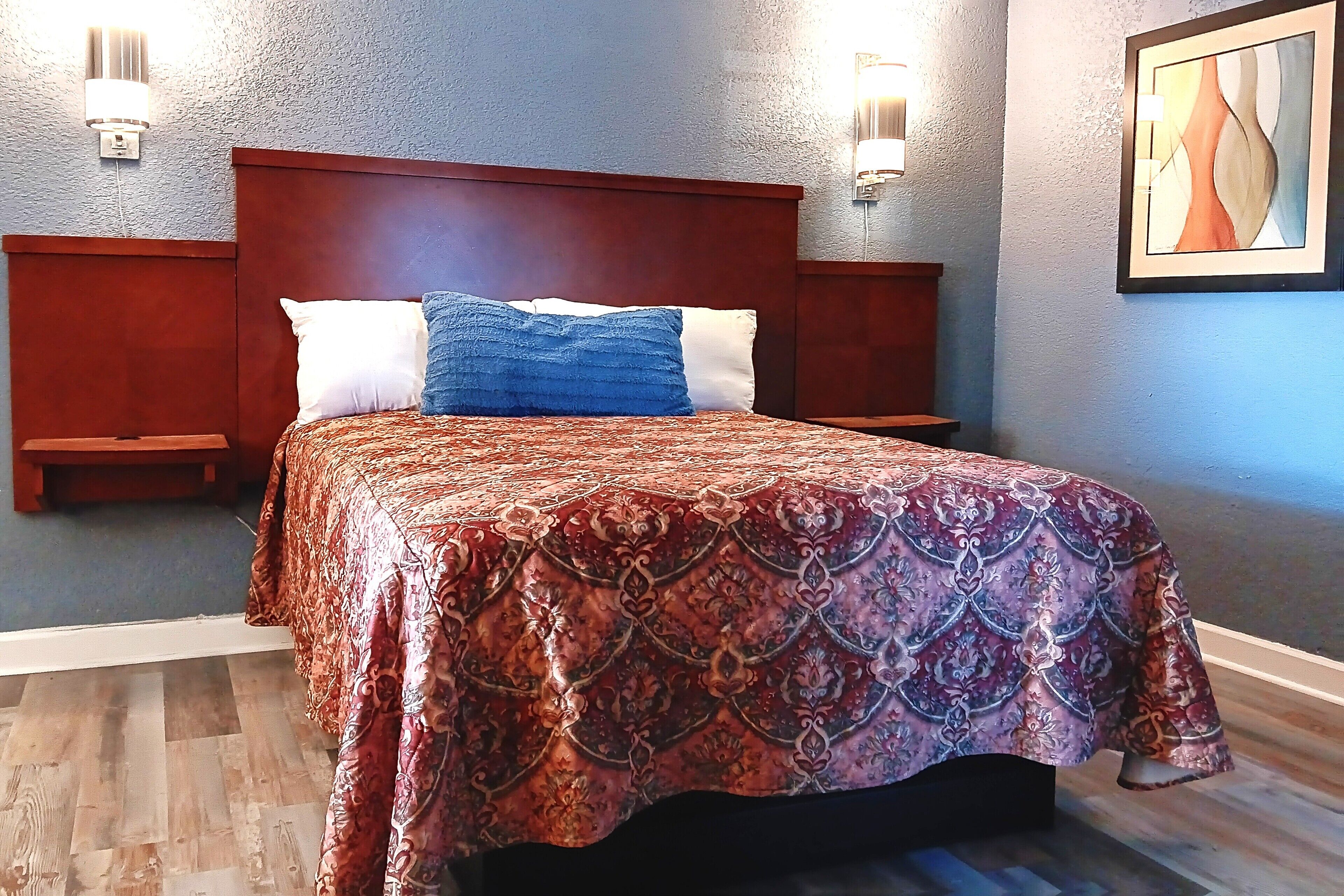 Un dormitorio con cabecera de madera, colcha estampada, dos mesitas de noche e iluminación en la pared.