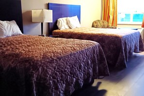 Two beds with brown quilts, a bedside lamp, and a window with curtains. - Sheldon's Motel by OYO Keysville Near Hwy 360 (Keysville)