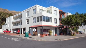 A multi-story hotel with a flat roof, large windows, and a red awning. - Anchor Bay (Cape Town)