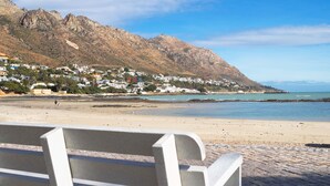 A beach with a rocky mountain in the background, a clear sky, and a bench in the foreground. - Anchor Bay (Cape Town)