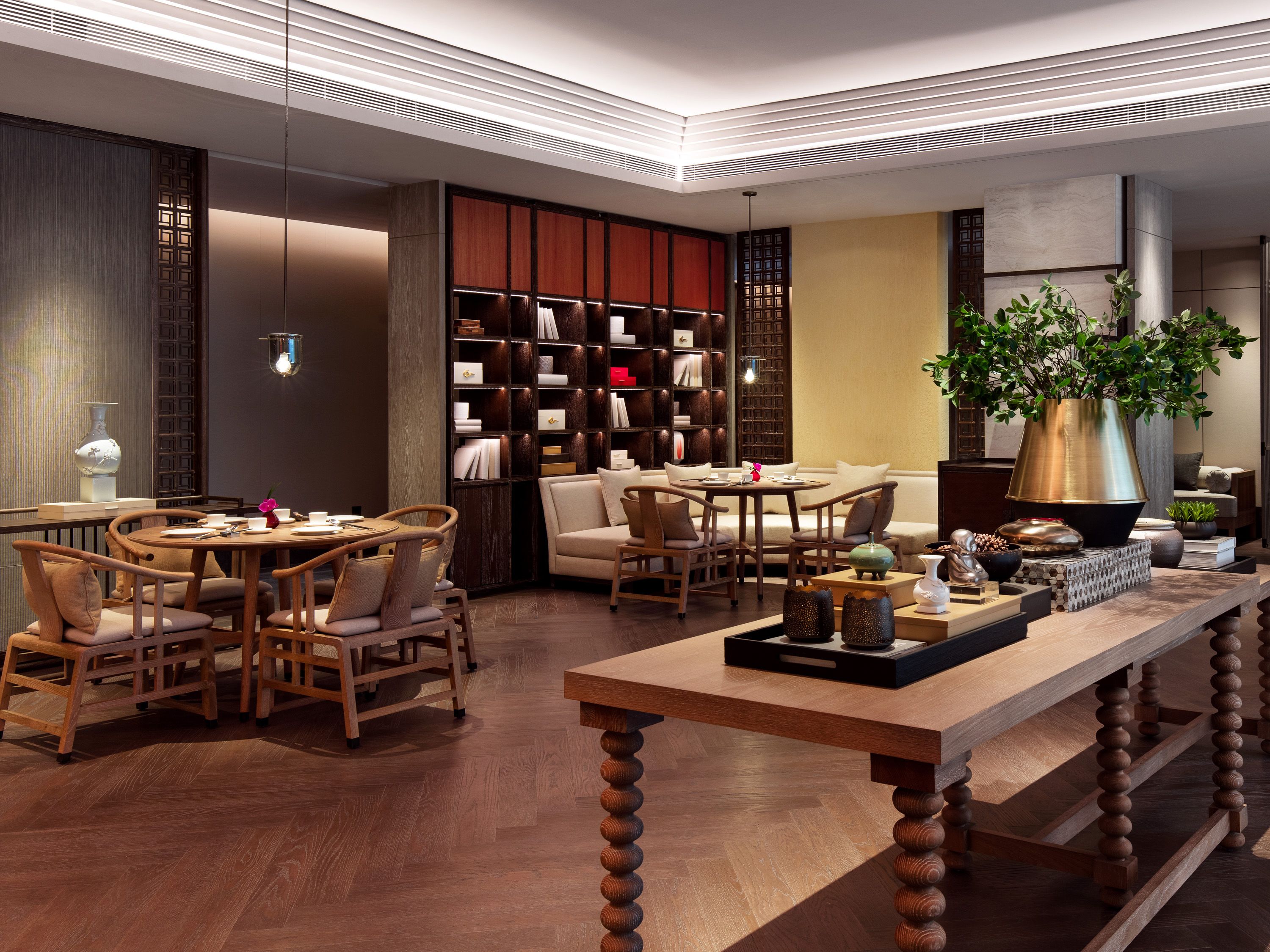 Un interior moderno con una mesa de comedor de madera, sillas, una estantería y una planta grande.